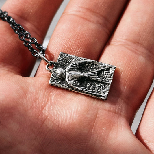 Silver pendant with a bird design held in a hand
