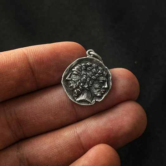 An oxidized sterling pendant featuring the Ancient Roman god with dual heads, held in a person's hand.