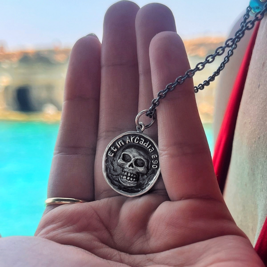 Hand holding a necklace with a skull pendant against a blurred outdoor background