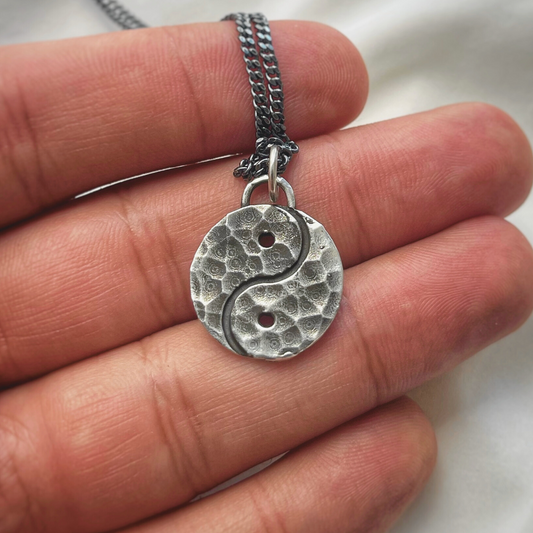 Silver yin yang pendant on a chain held between fingers
