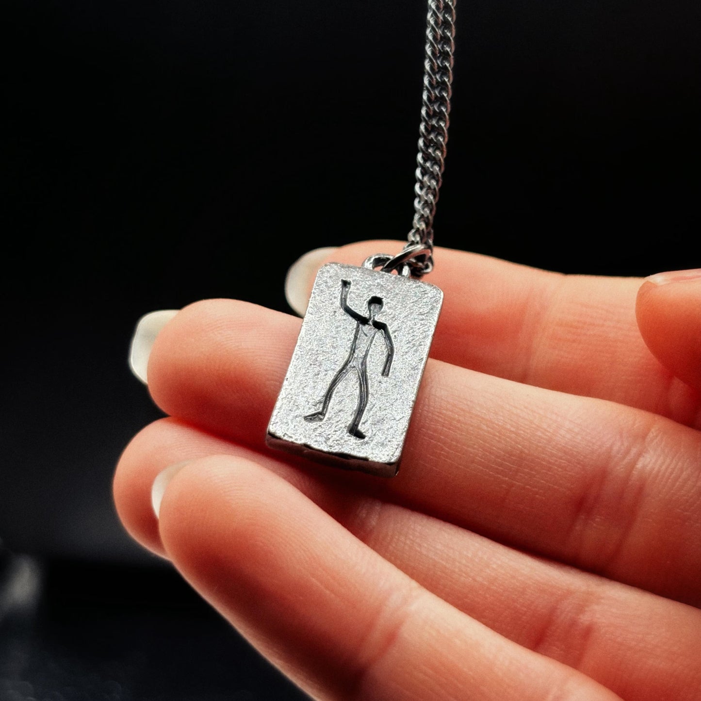 Silver pendant with a unique design held by a hand against a black background