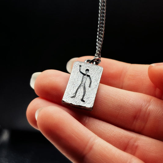 Silver pendant with a unique design held by a hand against a black background