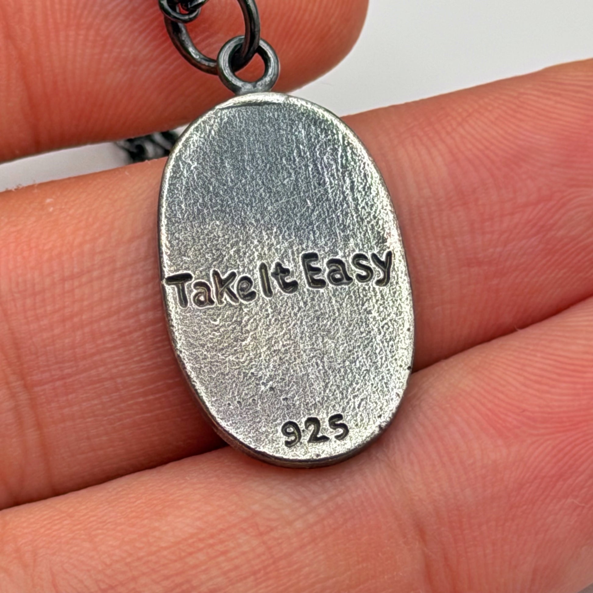 Silver pendant engraving held between fingers