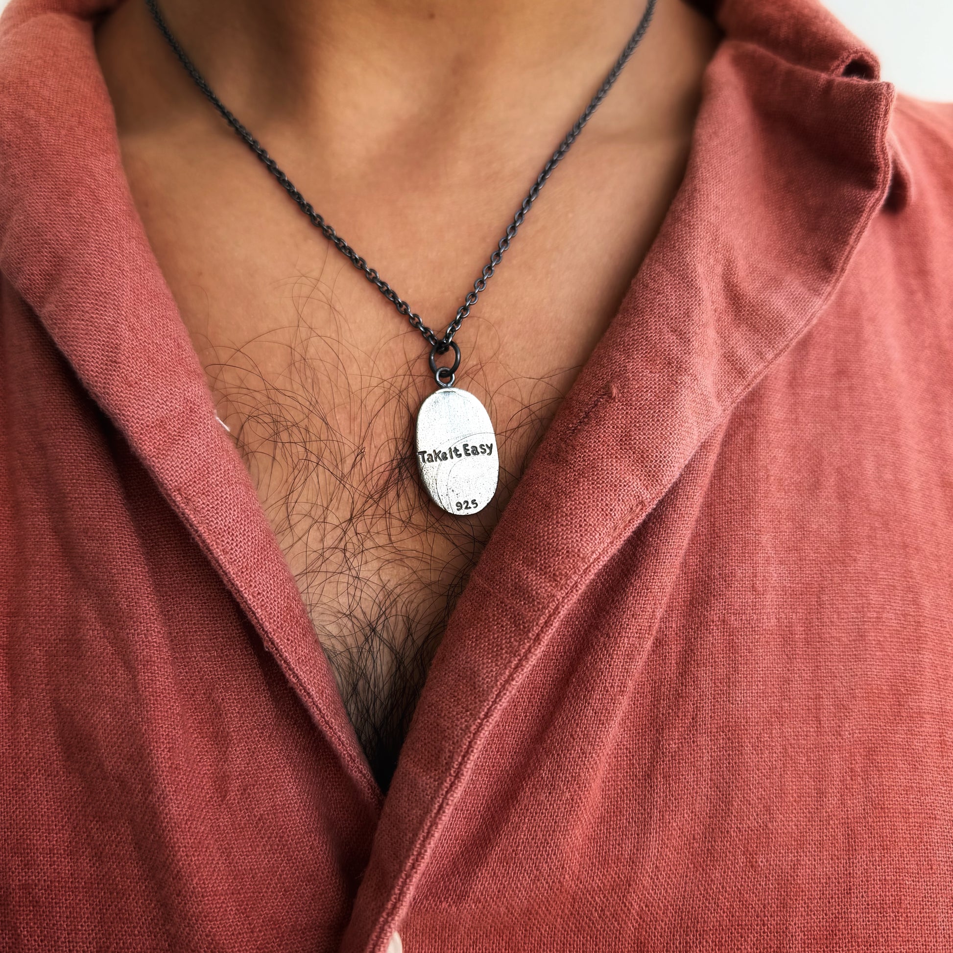 Person wearing a red shirt with a necklace featuring a pendant.