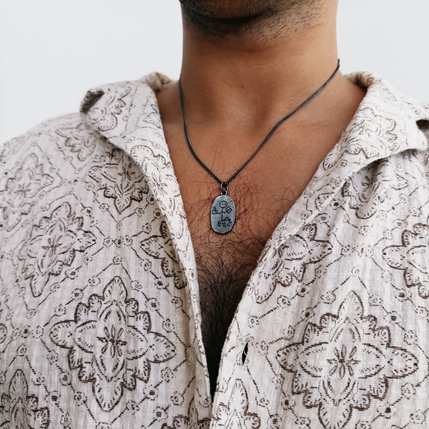 Person wearing a patterned shirt with a necklace featuring a pendant.