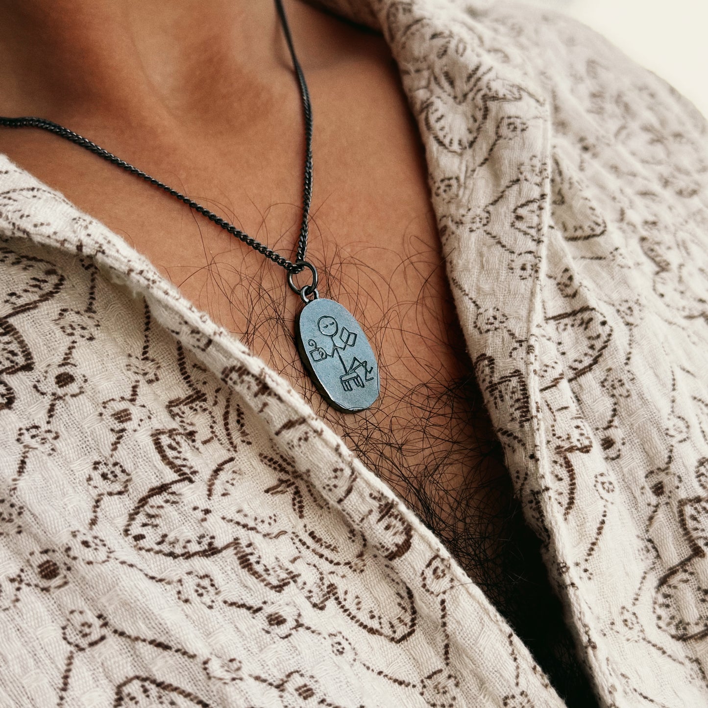 Necklace with a silver pendant worn by a person in a patterned garment