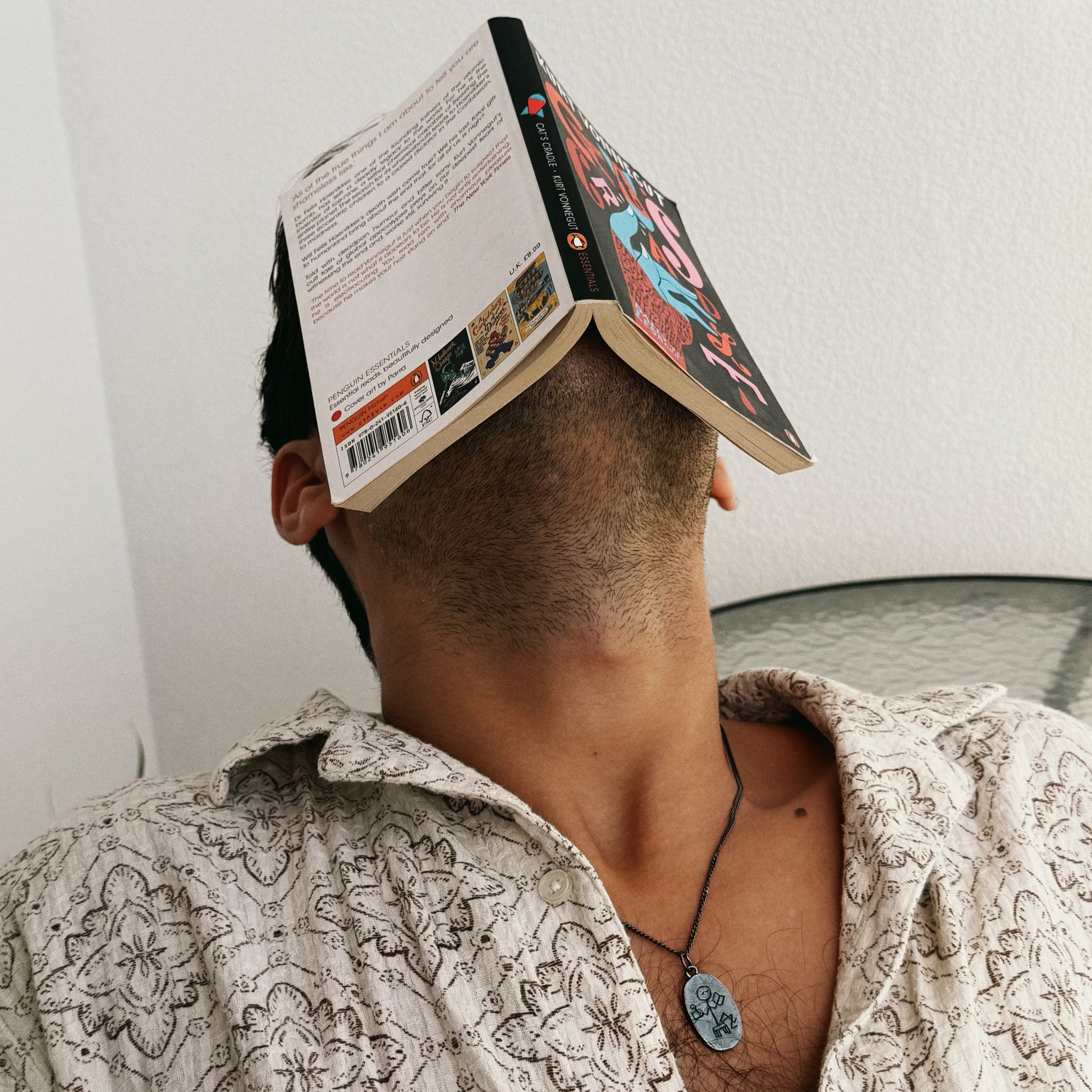 Person with an open book over their head, wearing a patterned shirt.