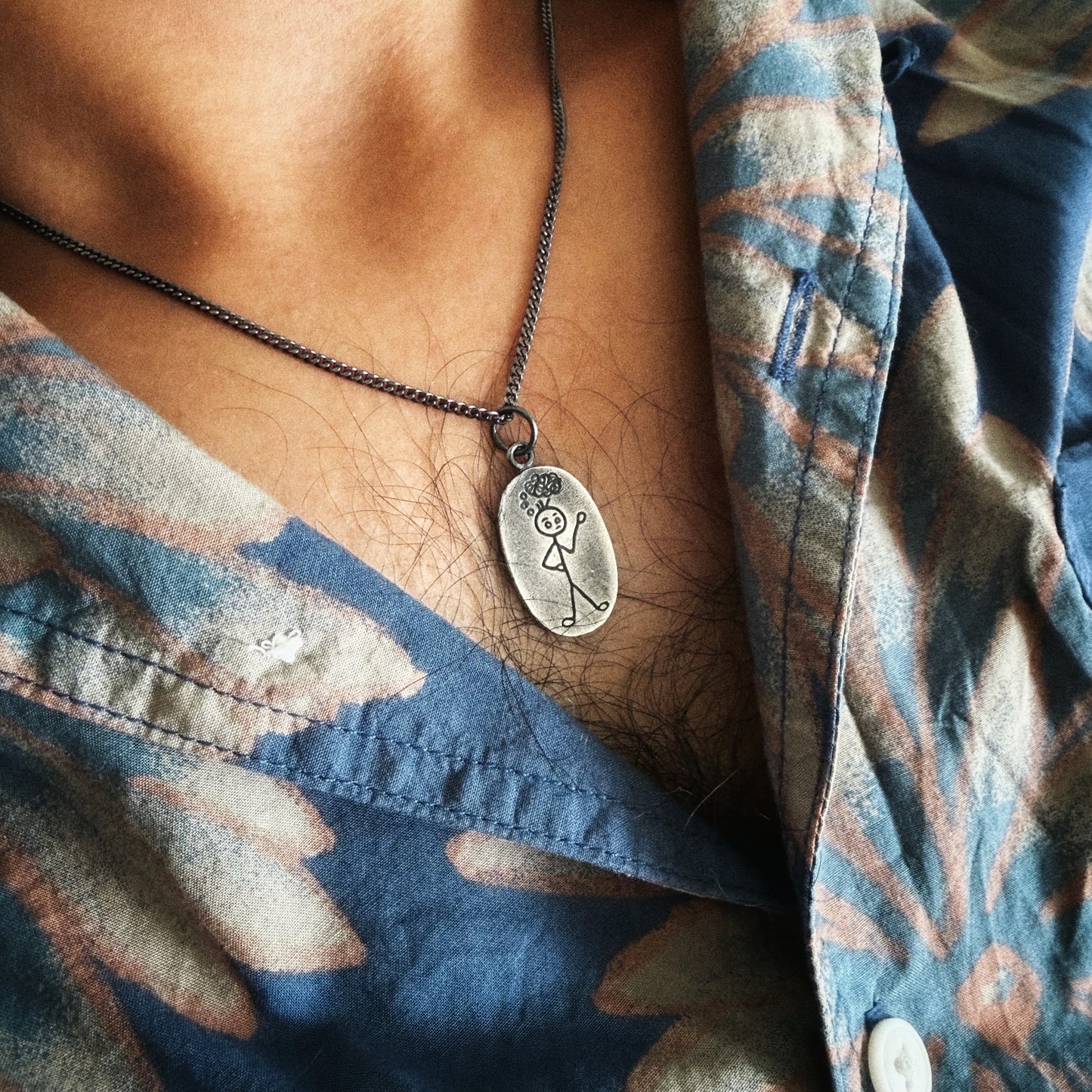 Necklace with a pendant worn by a person in a patterned shirt