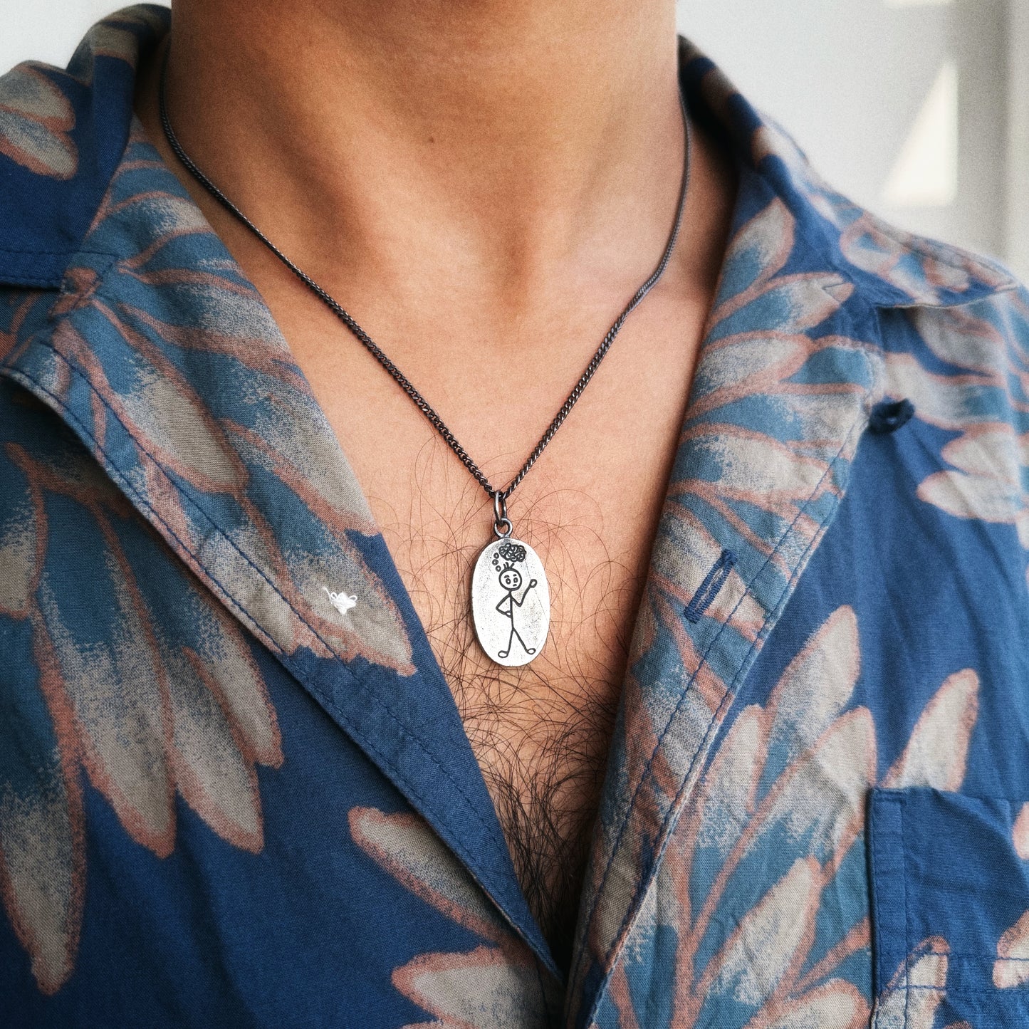 Person wearing a blue floral shirt with a necklace featuring a pendant.