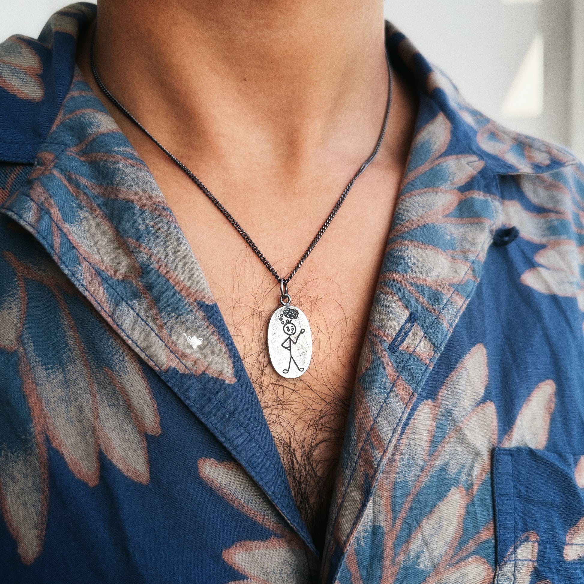 Person wearing a blue floral shirt with a necklace featuring a pendant.