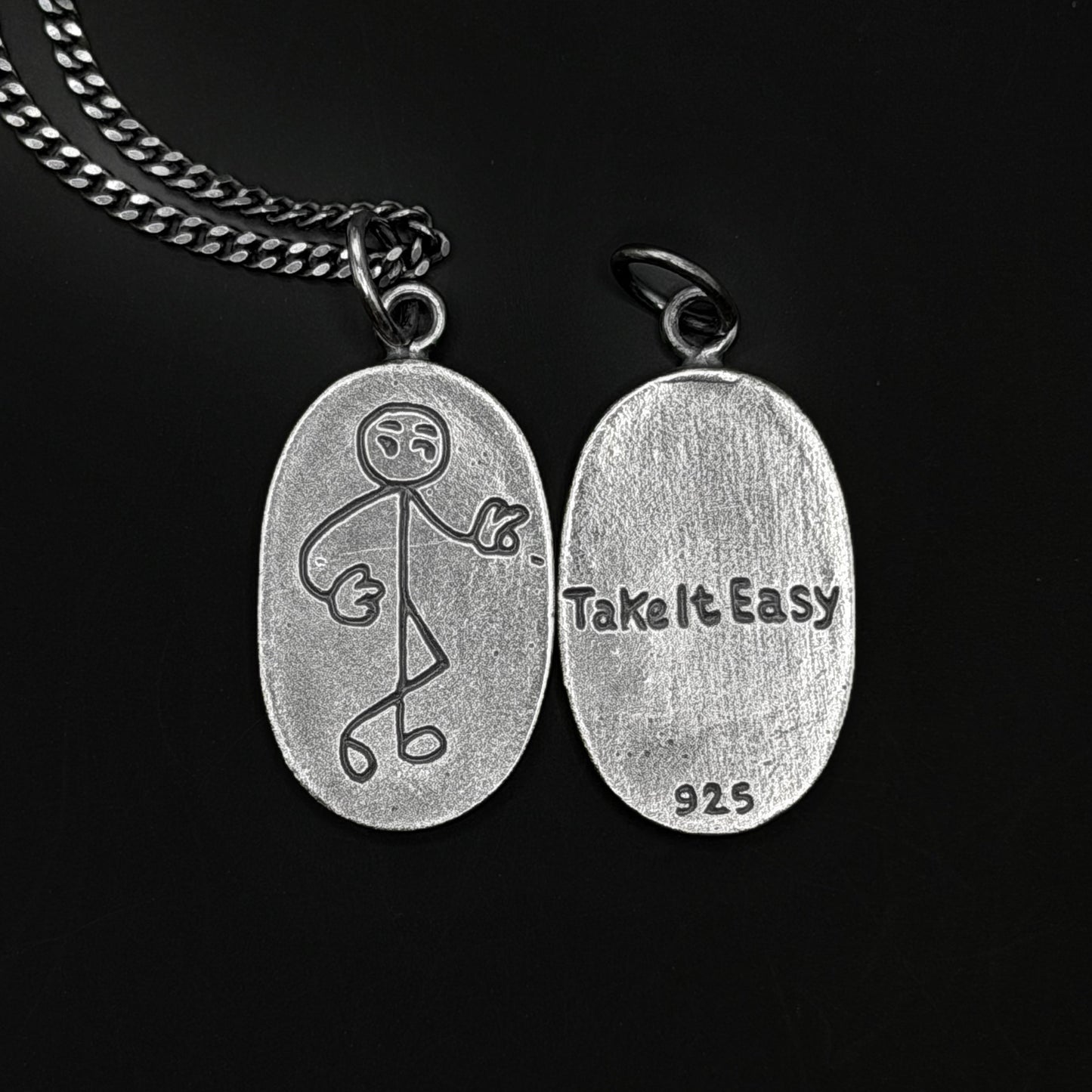 Silver pendant with stick figure design and 'Take It Easy' text on a black background