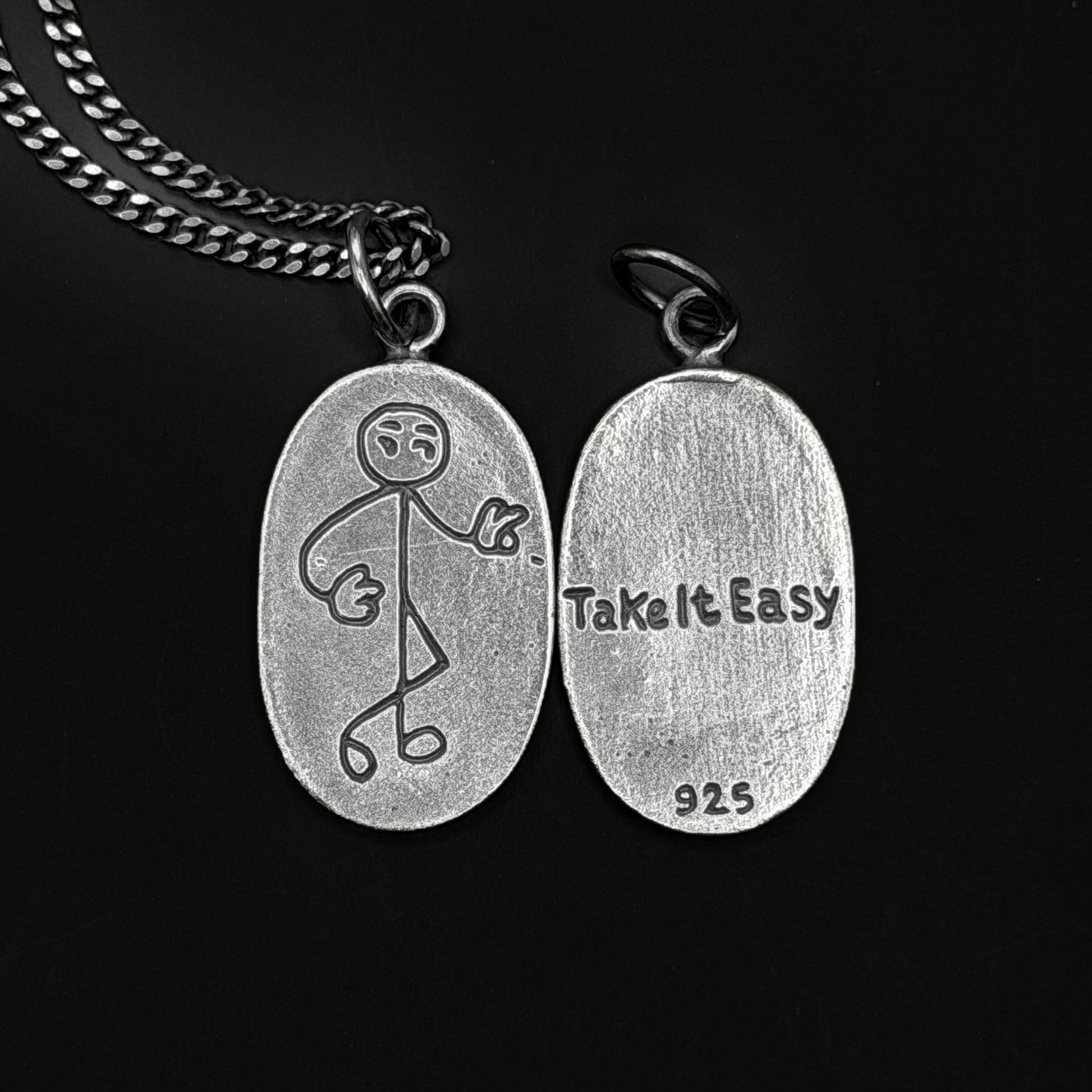 Silver pendant with stick figure design and 'Take It Easy' text on a black background