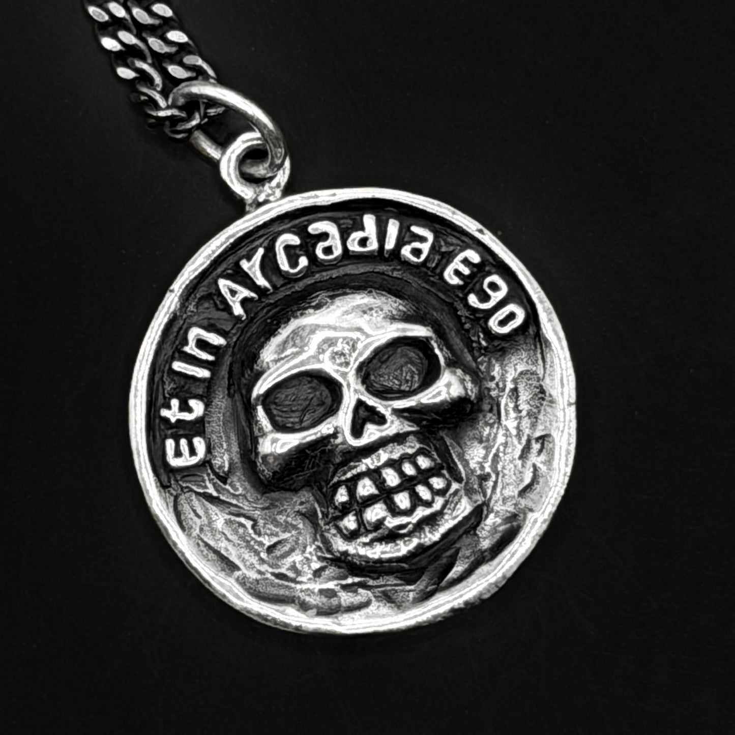 Silver pendant with skull design and 'Et in Arcadia Ego' text on a black background