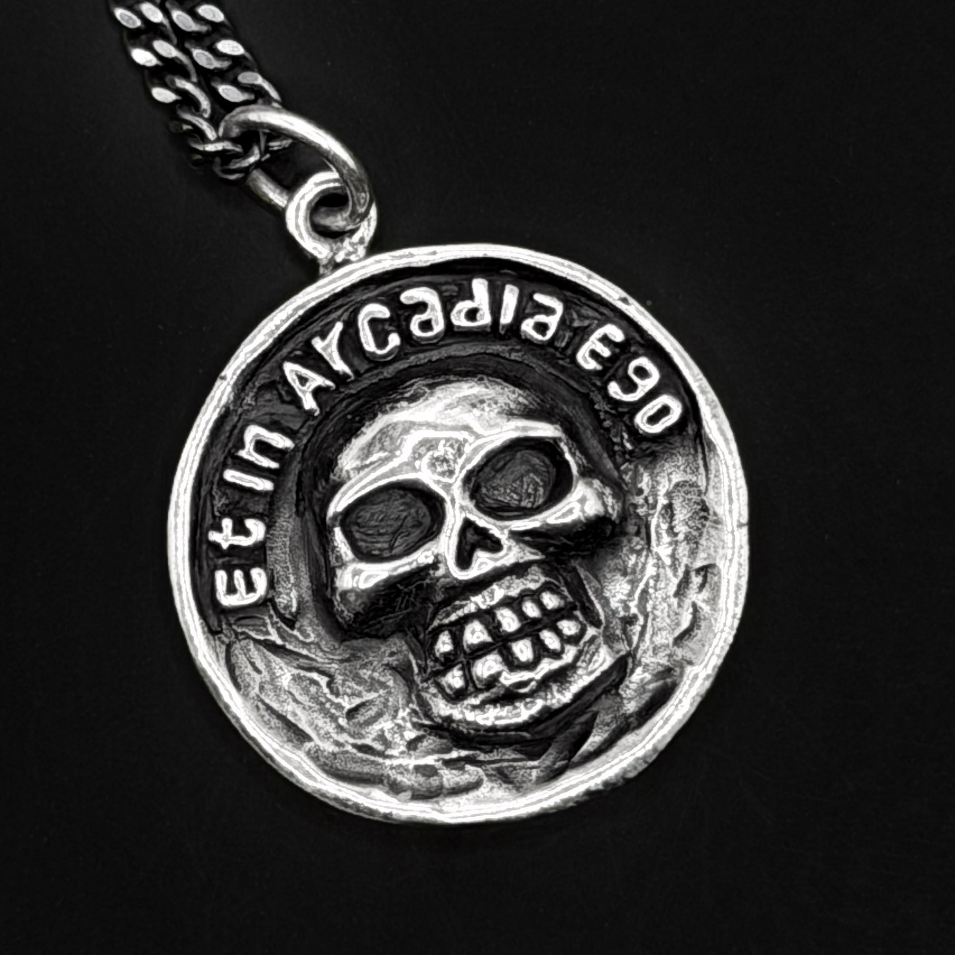 Silver pendant with skull design and 'Et in Arcadia Ego' text on a black background