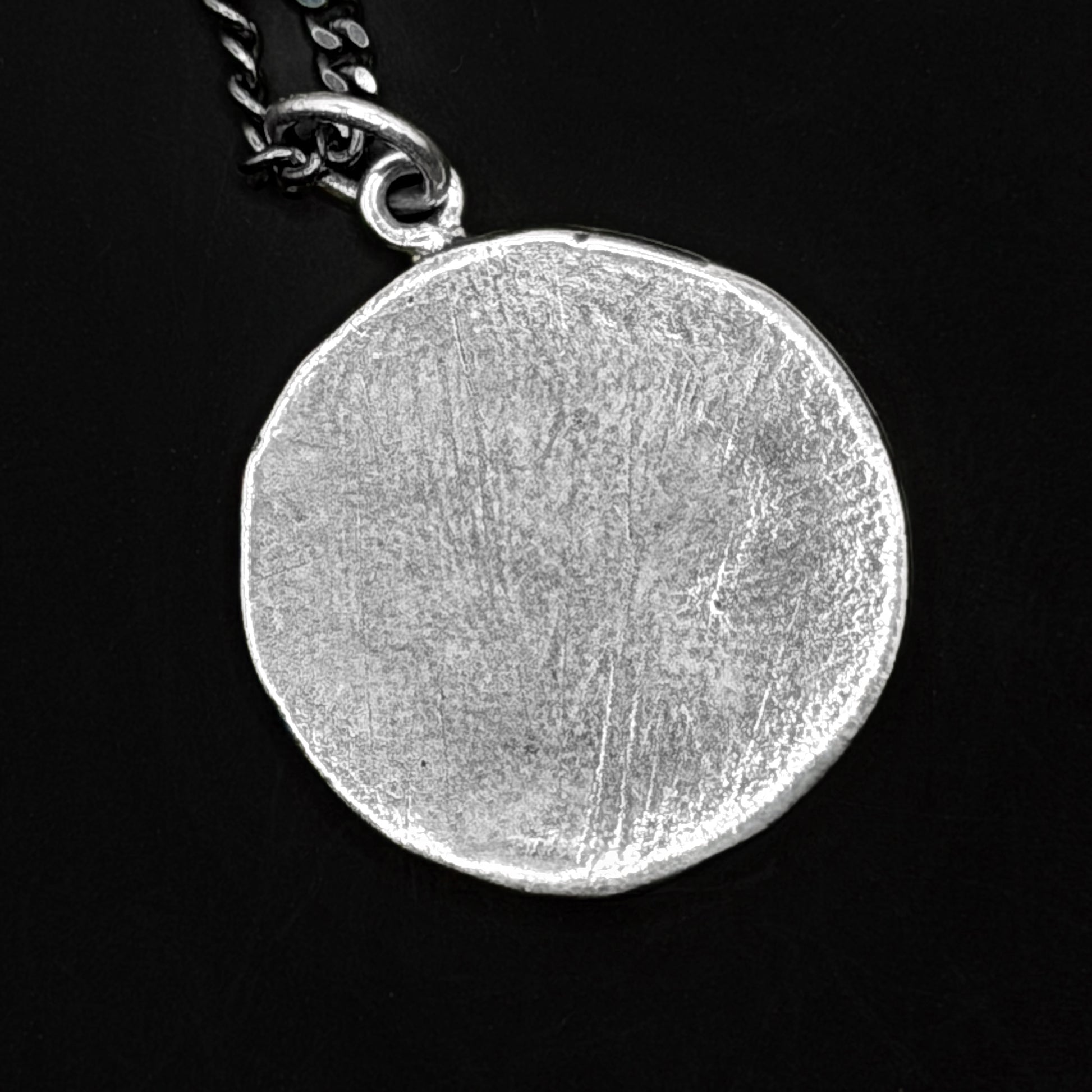 Silver circular pendant on a black background