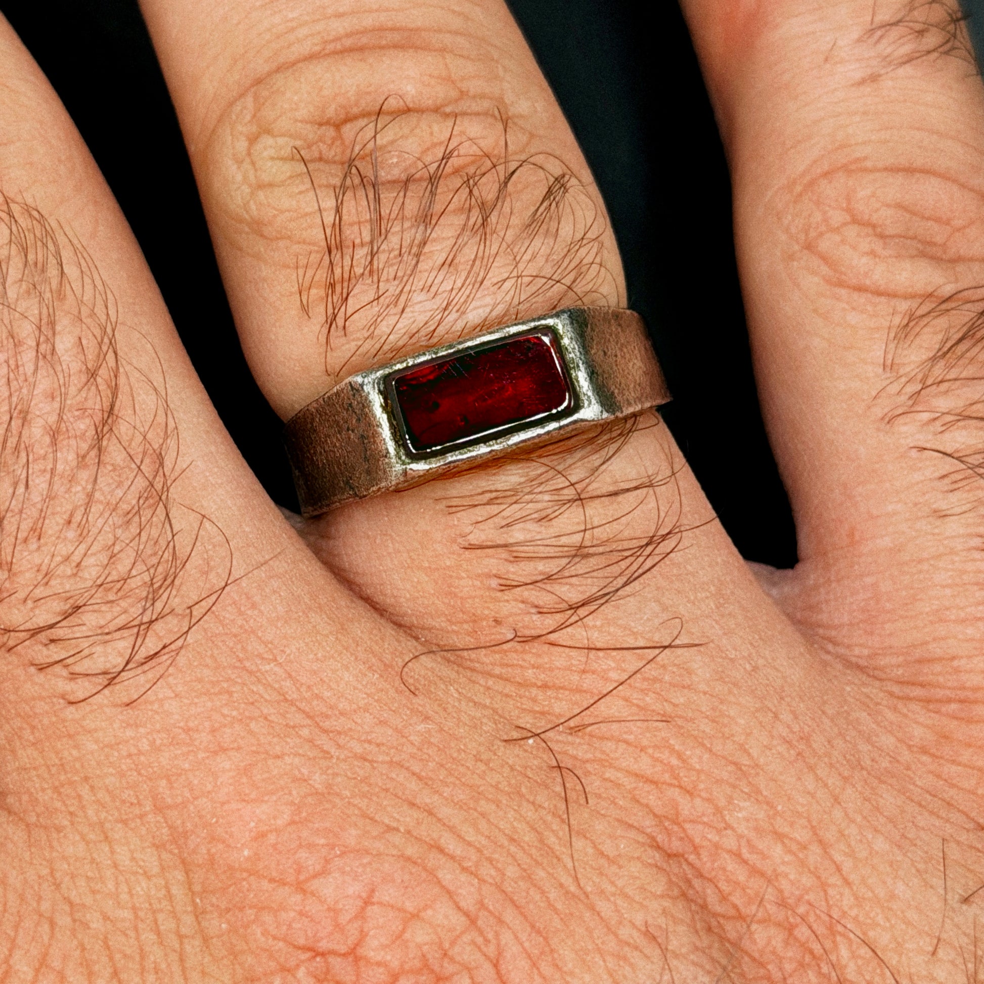 Close-up of a hand wearing a silver ring with a red stone on a dark background