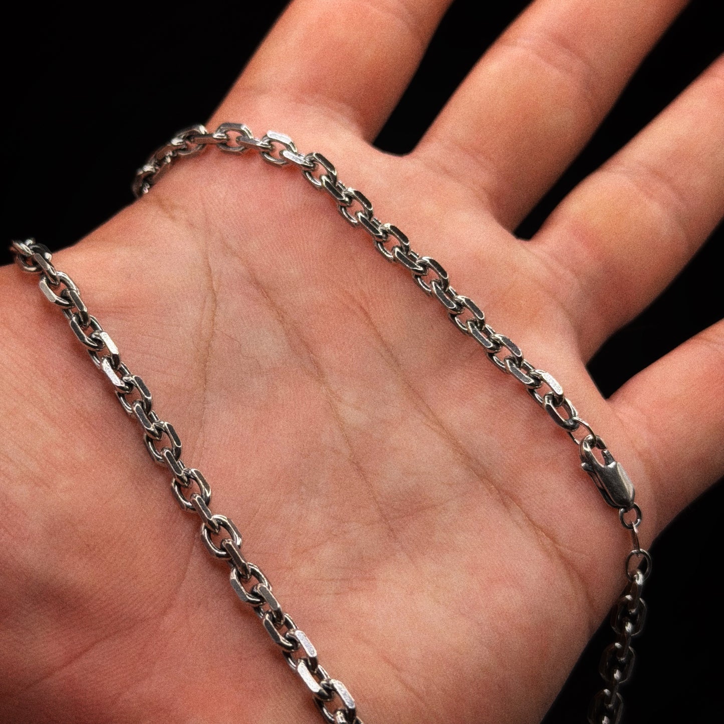 Silver chain necklace on a hand against a black background
