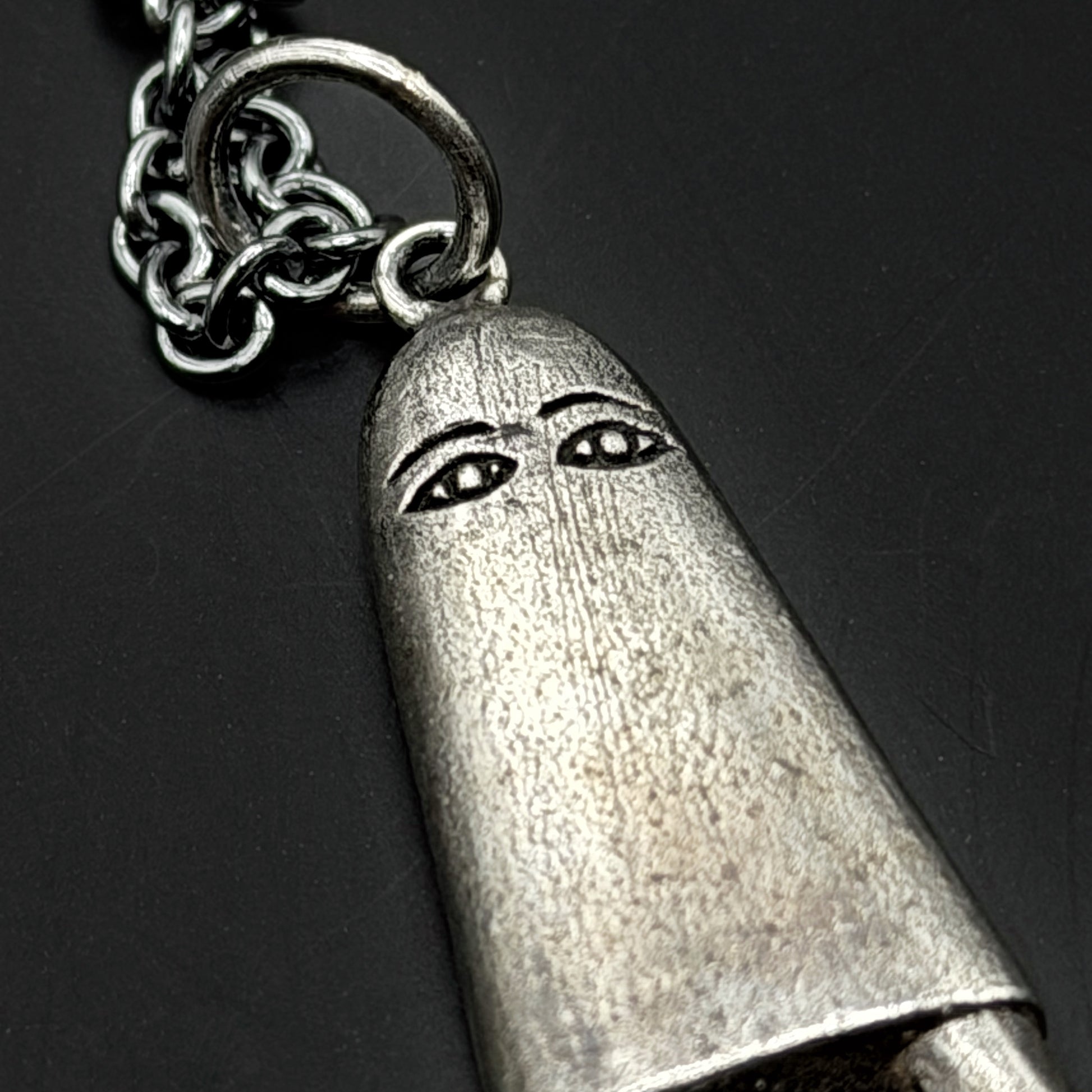 Silver bullet-shaped pendant with a face design on a dark background