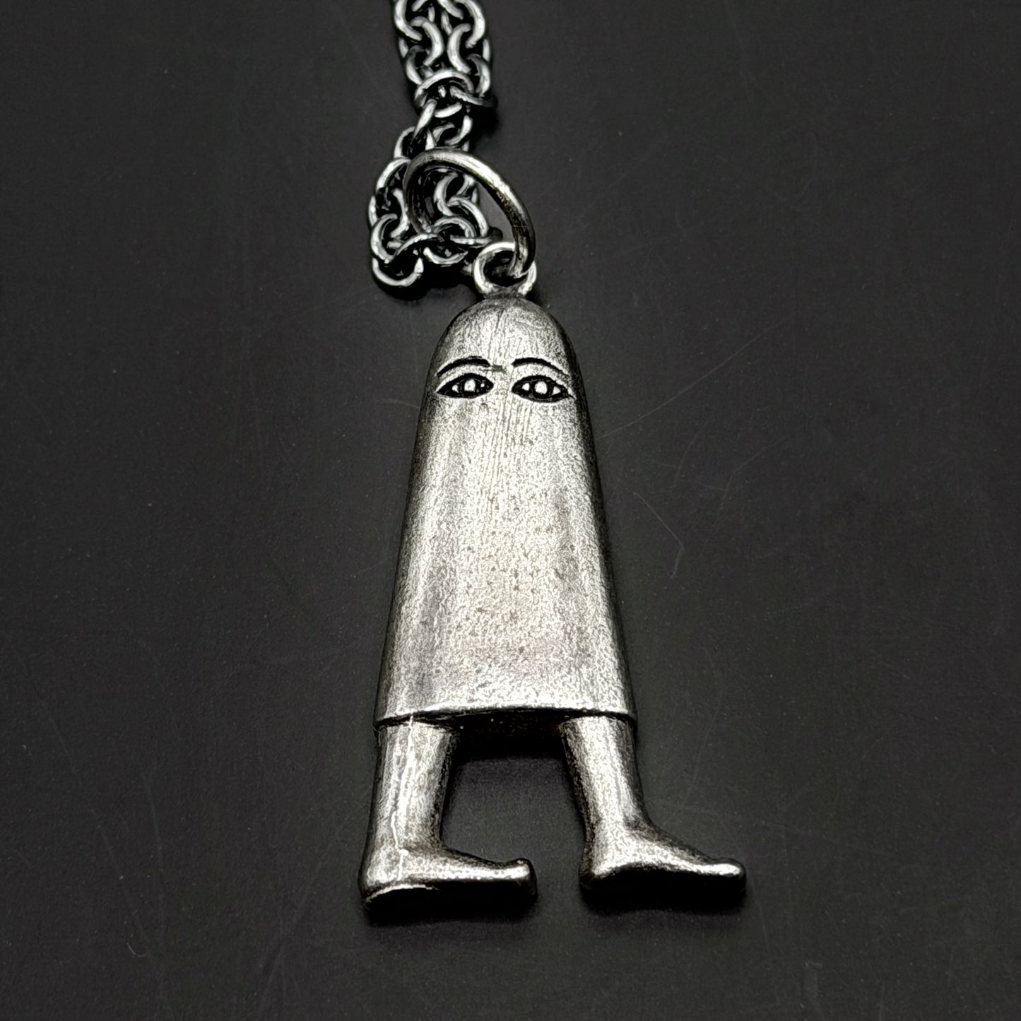 Silver pendant shaped like a person with a hood on a dark background