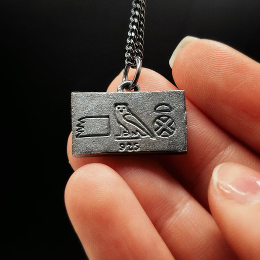 Silver pendant with hieroglyphics held by a hand against a black background
