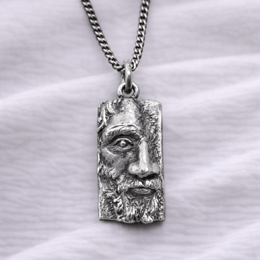 Silver pendant with a face design on a white fabric background