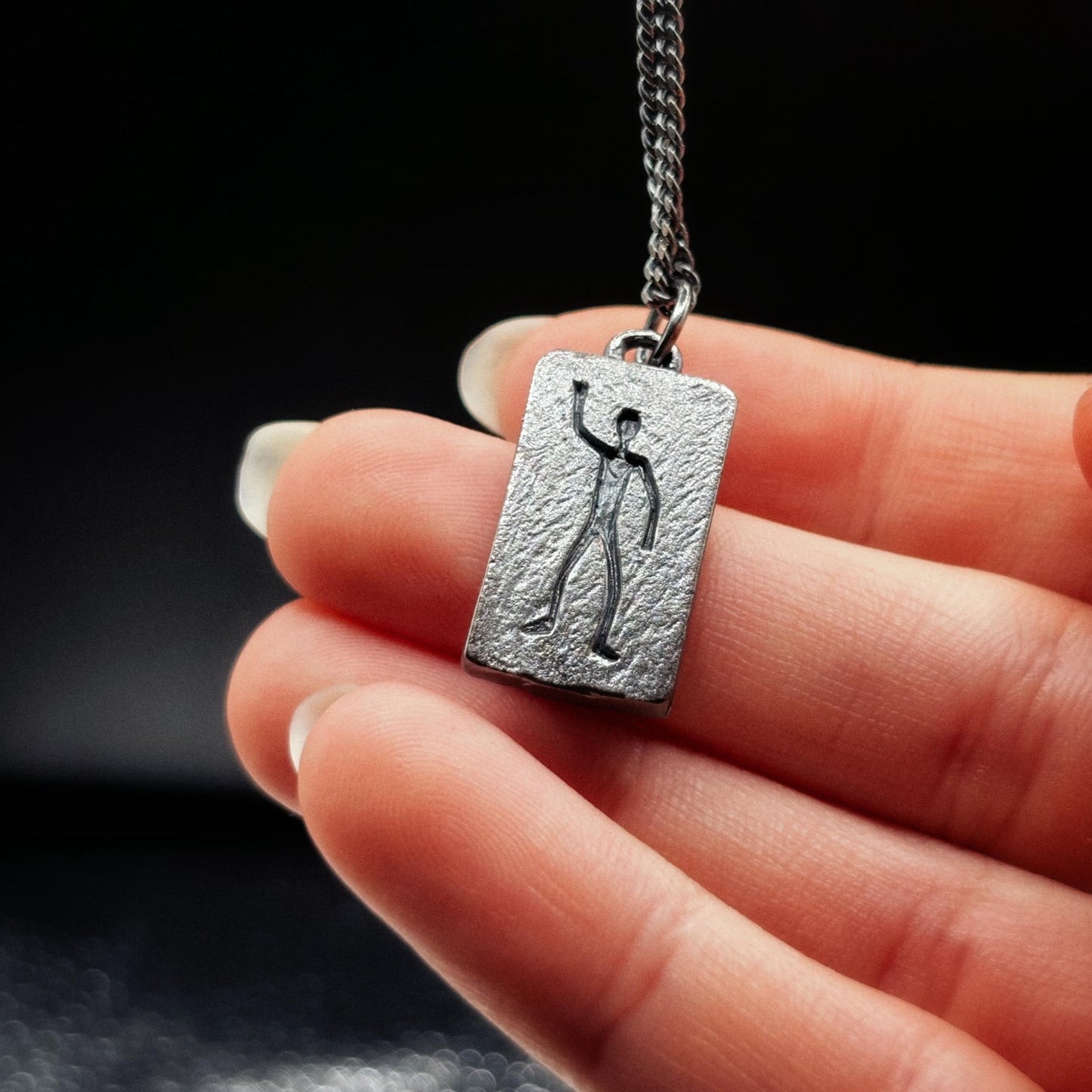 Silver pendant with a unique design held by a hand against a dark background