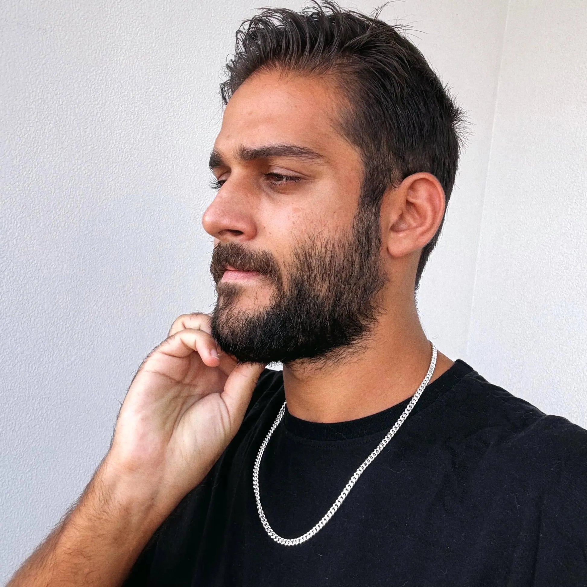 Man with a beard wearing a black shirt and silver chain, against a plain background