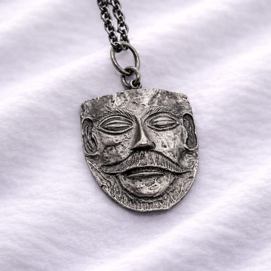 Silver pendant with face design on a white fabric background