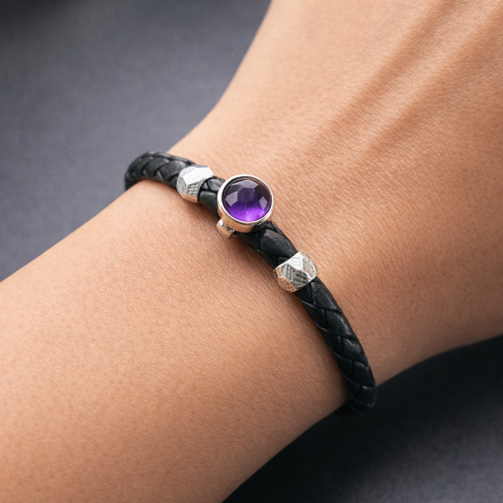 Black braided bracelet with a purple gemstone on a wrist against a dark background
