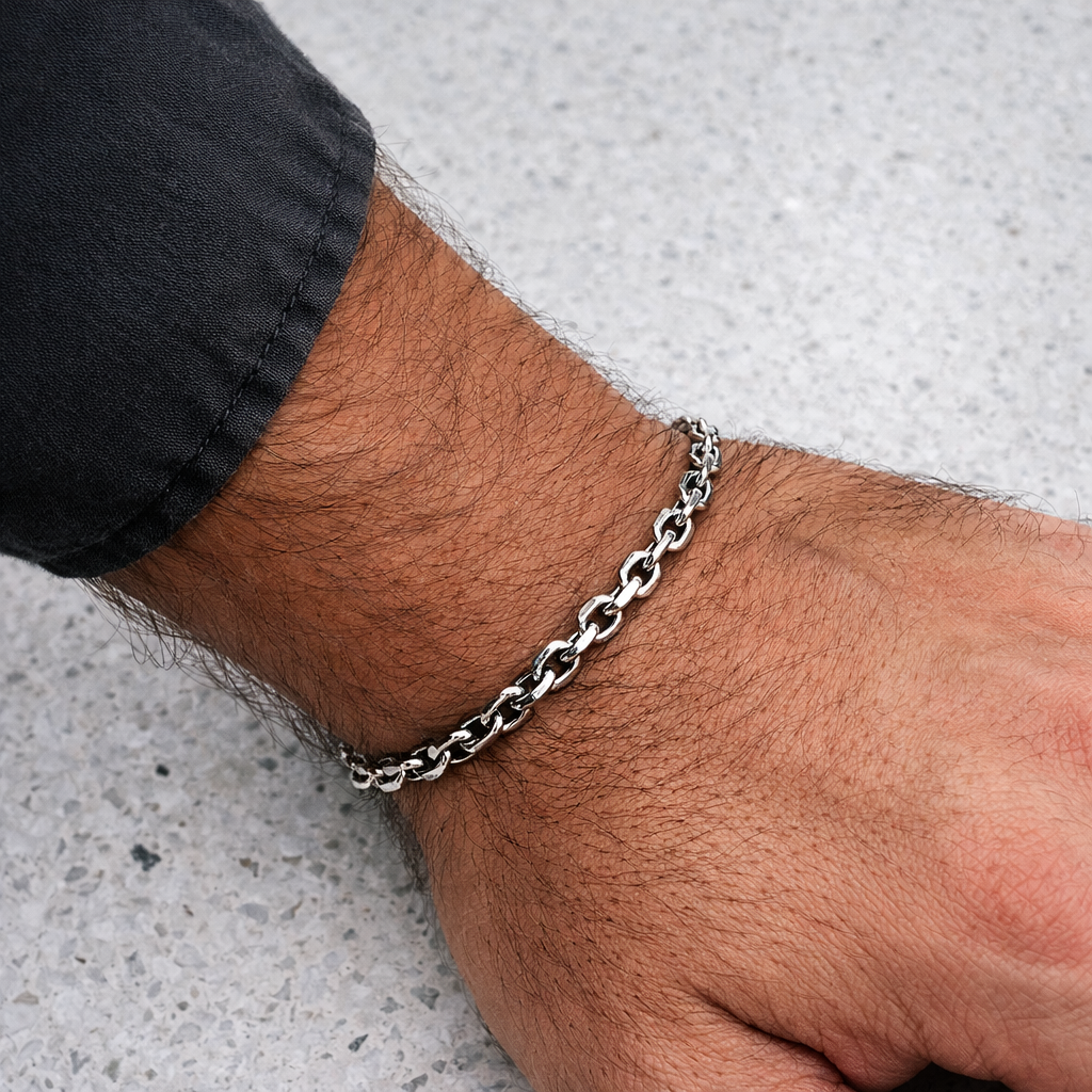 Close-up of a person's wrist wearing a silver chain bracelet on a light gray background