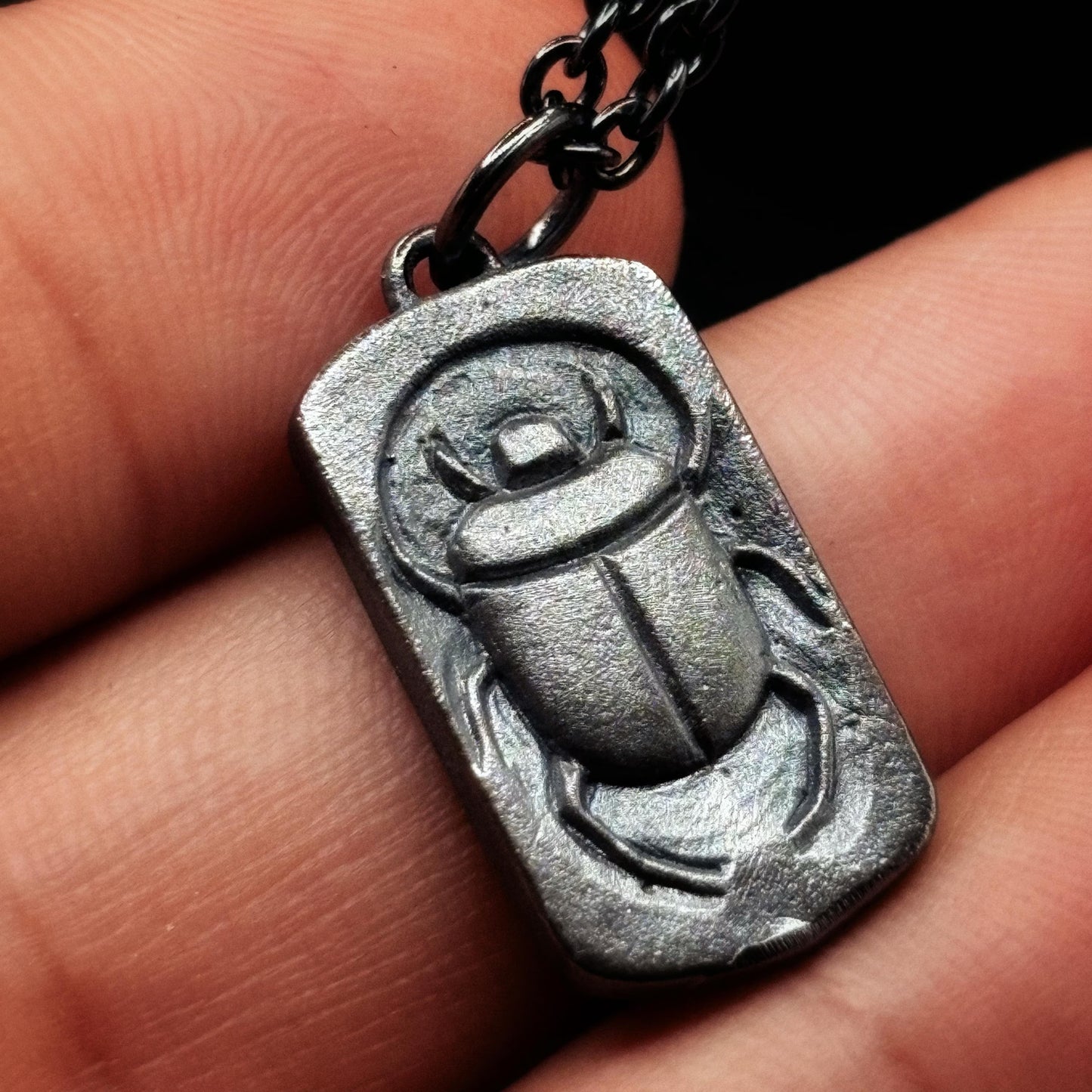 Silver scarab pendant on a chain held between fingers