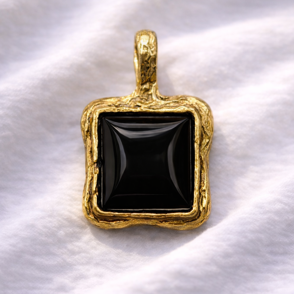 Gold pendant with a black stone on a white fabric background