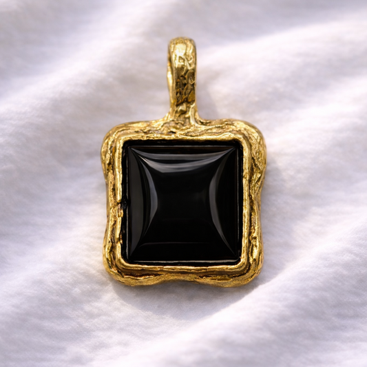 Gold pendant with a black stone on a white fabric background
