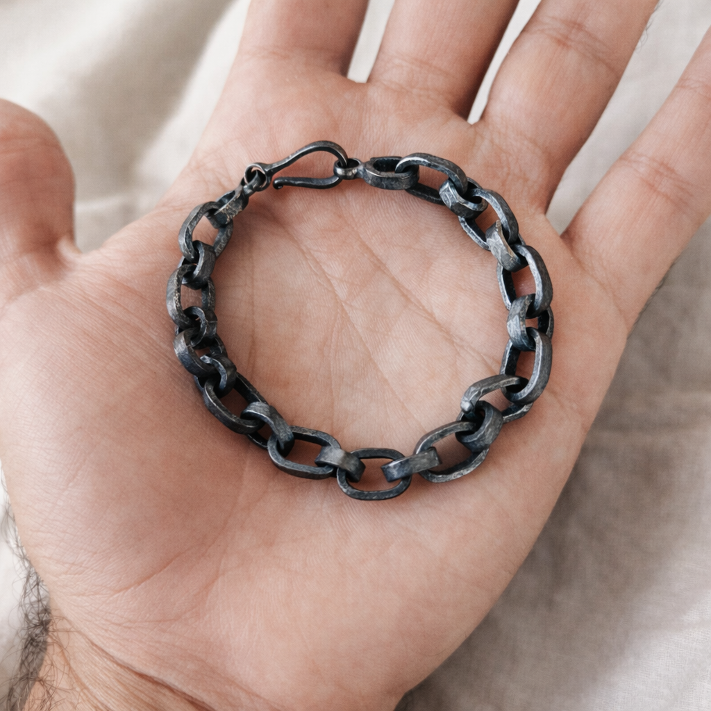 Hand holding a black chain bracelet against a neutral background
