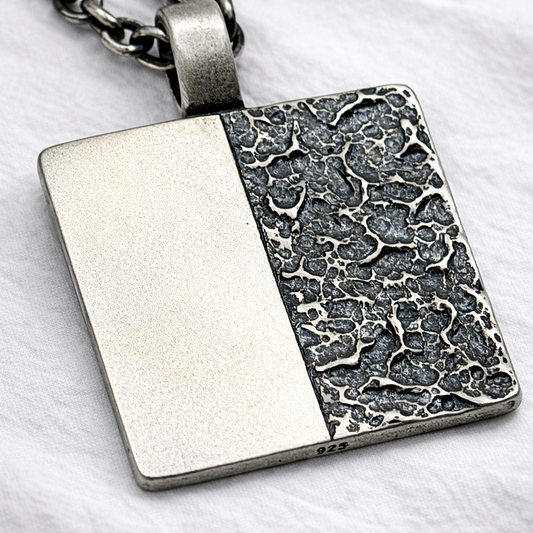 Silver pendant with textured design on a white background