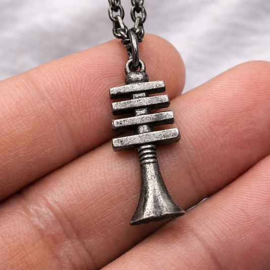 Silver necklace pendant held between fingers against a neutral background