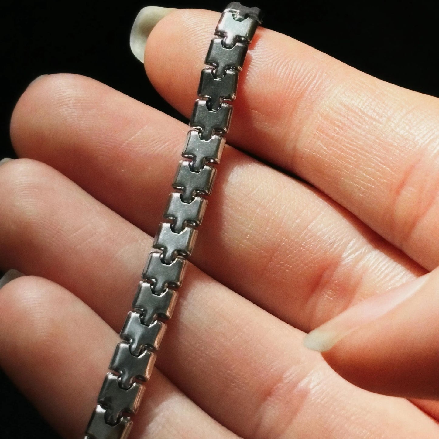 Close-up of a hand holding a silver chain bracelet against a black background