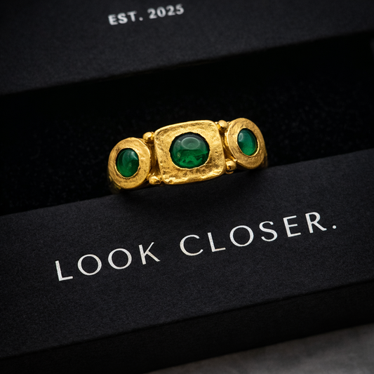 Gold ring with green gemstones on a black background with 'Look Closer' text