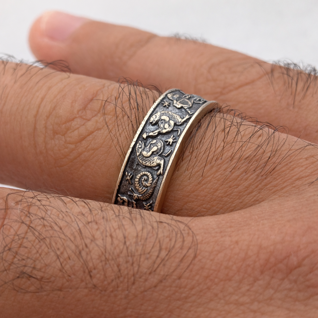 Silver ring with intricate designs on a person's finger against a neutral background