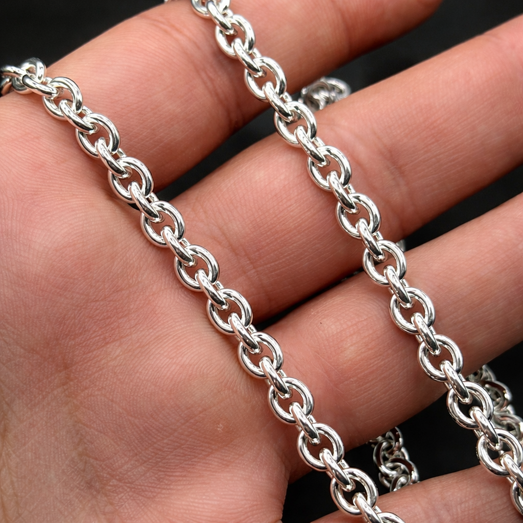 Silver chain held in a hand against a black background