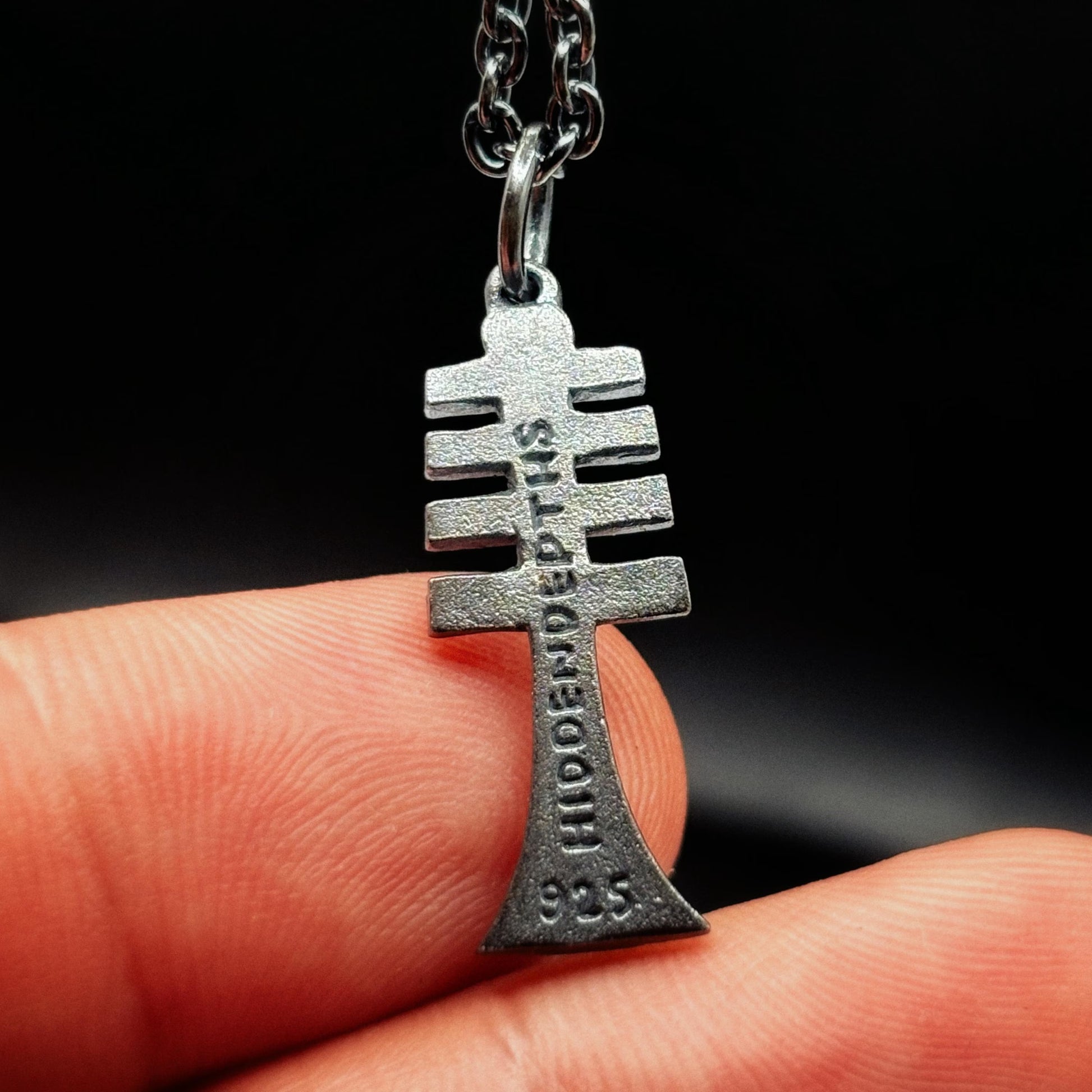 Silver pendant with 'HIDDENDEPTHS' branding held between fingers against a dark background