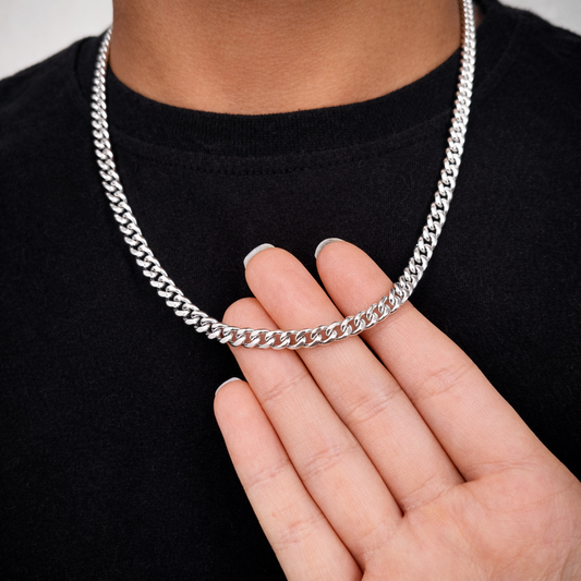 Silver chain necklace held by a hand against a black background