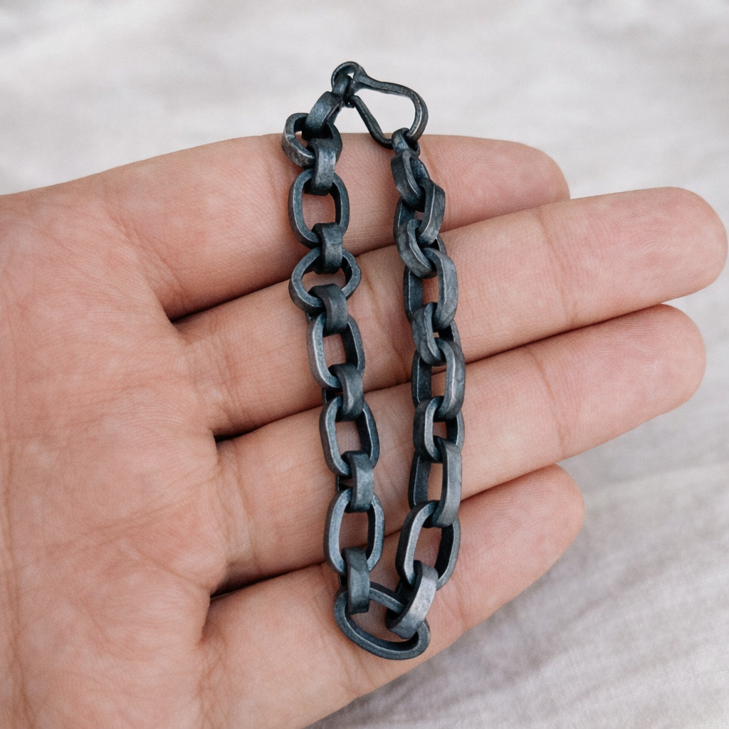 Hand holding a black chain bracelet against a neutral background