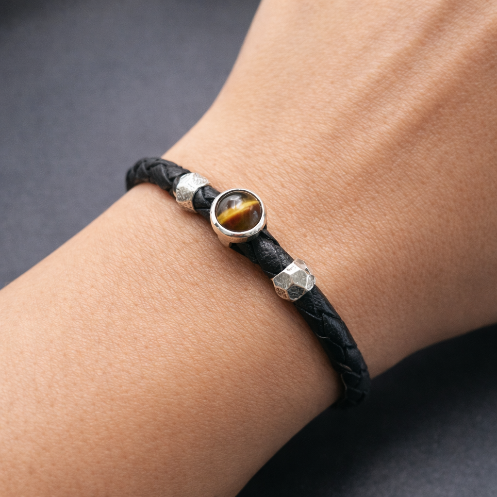 Black leather bracelet with a tiger eye stone and silver beads on a wrist against a dark background