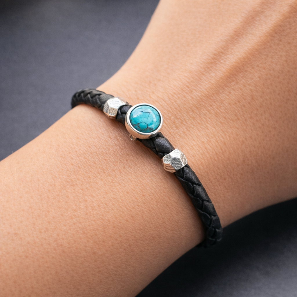 Bracelet with black leather strap, turquoise stone, and silver beads on wrist against a dark background