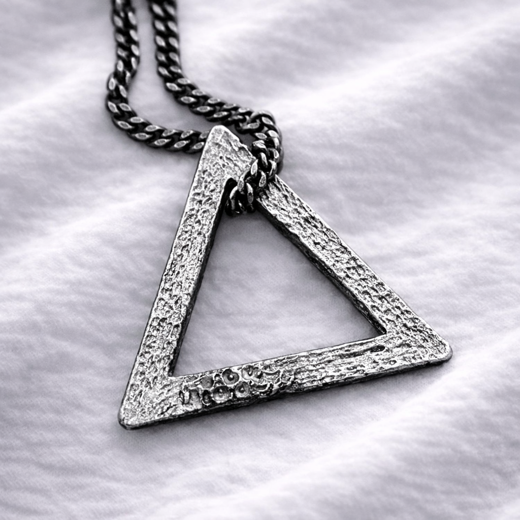 Silver triangle pendant necklace on a white fabric background